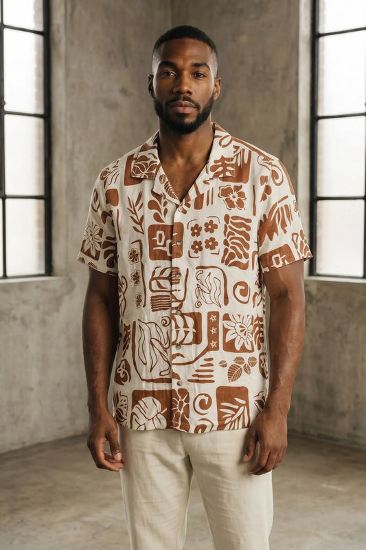 Man wearing a patterned shirt standing in a room with large windows.
